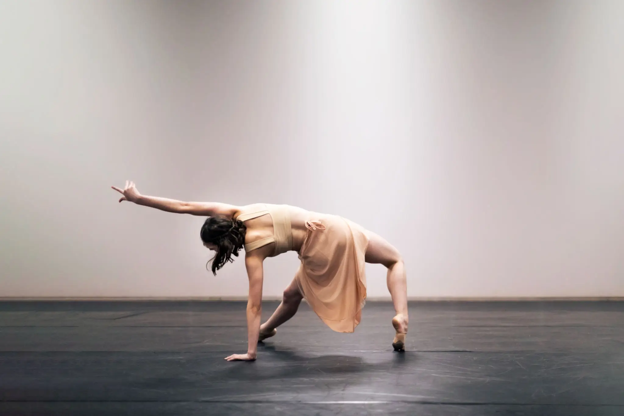 Dancer in a beige dress performing a backbend on stage.