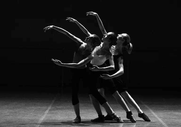 Three ballet dancers in mid-motion on stage with dramatic lighting.